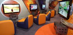 an orange and blue room with two televisions on the wall, some chairs in front of them