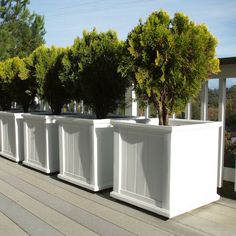 several white planters are lined up on the side of a wooden deck near trees