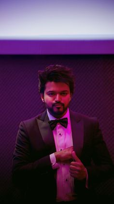 a man in a tuxedo and bow tie is posing for the camera with his hand on his chest