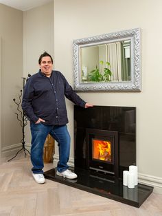 a man standing in front of a fireplace with a mirror on the wall above it