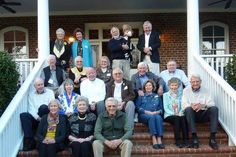 a group of older people sitting on the front steps of a house, posing for a photo