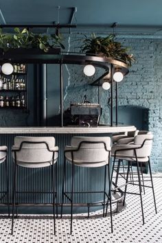 a bar with stools and plants on the back wall in a room that has blue brick walls