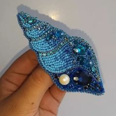 a hand holding a blue brooch with pearls and beads on it's side