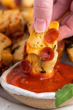 a person dipping some food into a bowl with tomato sauce and cheese on the side