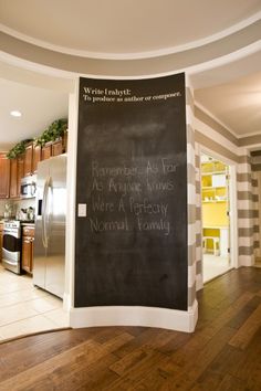 a chalkboard sign in the middle of a kitchen with wood floors and cabinets on either side