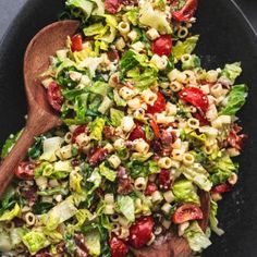 a wooden spoon filled with salad on top of a black plate topped with lettuce and tomatoes