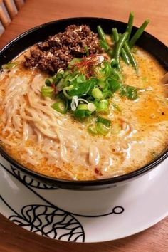 a bowl of soup with noodles, green onions and meat in it on a plate