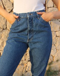 Mom jeans in dark blue. High rise. Zipper fly. Front and back pockets. Tapered leg. Extra long leg. Size EU 40 / UK 12 Actual measurements - 30"(76cm) waist - 38"(97cm) hips - 33"(84cm) inner leg - 12.5"(32cm). Composition - 100% Cotton Condition - Excellent. Sustainability - Vintage Handpicked, repaired and ready to wear. This is an original vintage item, not new and minor signs of wear and age are expected, we will highlight any major flaws. Model is a size UK 6/8 and is 5'7" tall Dark Wash Wide Leg Bottoms With Zip Fly, Dark Wash Mid-rise Pants With Zip Fly, Mid-rise Dark Wash Pants With Zip Fly, Denim Blue Jeans With Zip Fly In Rigid Denim, Denim Blue Jeans With Hip Pockets, Full-length Denim Blue Jeans With Hip Pockets, High Waist Dark Wash Pants With Zip Fly, Full Length Denim Blue Jeans With Hip Pockets, Dark Wash Mid-rise Jeans With Hip Pockets