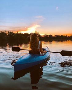 a woman sitting in a blue kayak on the water at sunset with her back to the camera