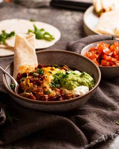 a bowl filled with food sitting on top of a table next to other plates and utensils