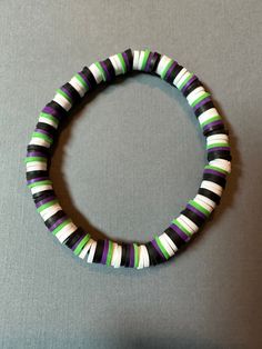 a black, white and green beaded bracelet on a gray surface with a silver clasp