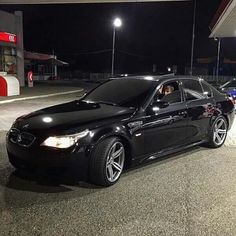 a black car parked in front of a gas station at night with its lights on