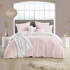 a bed with pink sheets and pillows in a room next to a white rug on the floor