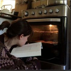 a woman reading a book in front of an oven