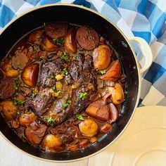 a pot filled with meat and potatoes on top of a blue and white checkered table cloth