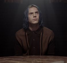 a man with blue hair sitting at a table in front of a light that is on