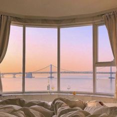 a bedroom with a large window overlooking the water and bridge in the distance at sunset