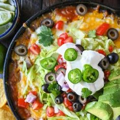 a pizza topped with black olives, cheese and green peppers next to tortilla chips