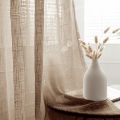 a vase with some flowers in it sitting on a table next to a window curtain