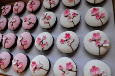 cupcakes decorated with pink and white frosting are in a cardboard box on a table