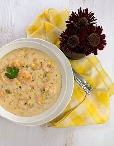 a bowl of soup with shrimp, corn and garnish next to a flower