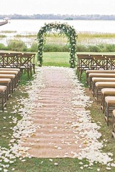 an outdoor ceremony setup with wooden chairs and white petals on the aisle, along with greenery