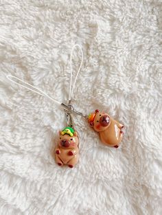 two small ceramic animals hanging from a silver hook on a white background with tiny beads