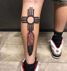 a person with a tattoo on their leg that has an arrow in the center and a native american feather