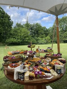 an outdoor table with many different types of food on it, including cheeses and fruit