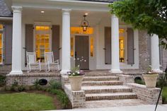 the front porch of a house with white pillars and two chairs on it's steps