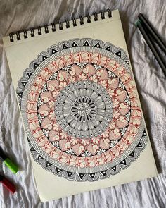 a notebook with an intricate design on the cover next to markers and pencils in front of it