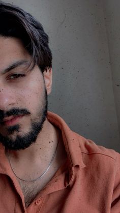 a man with long hair and beard wearing an orange shirt looking off to the side