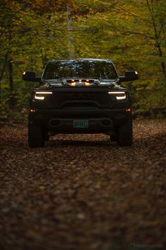 the front end of a black truck driving down a forest road