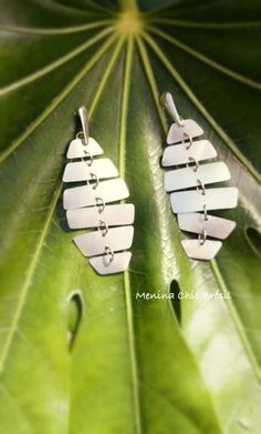 pair of silver earrings on top of a green leaf with the word love written in it