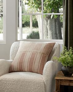 a white chair sitting in front of a window next to a potted plant on top of a wooden table