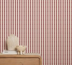 a white vase sitting on top of a wooden table next to a red and white striped wall