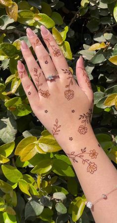 a woman's hand with tattoos on it and leaves around her wrist, in front of some bushes