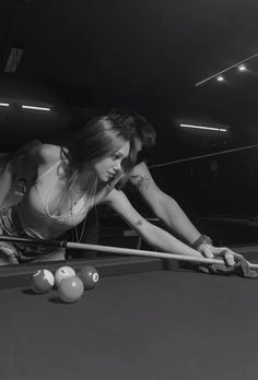 a woman is leaning over to hit a pool ball with her racket and cues