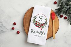 a personalized dish towel with a monogrammed christmas wreath on it and a red handled utensil