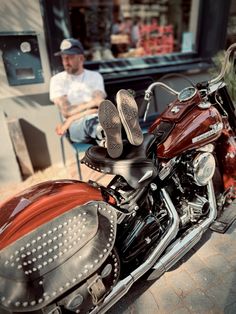 a red and black motorcycle parked in front of a building next to a man sitting on a chair