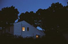 a white house is lit up at night with trees in the foreground and dark blue sky behind it