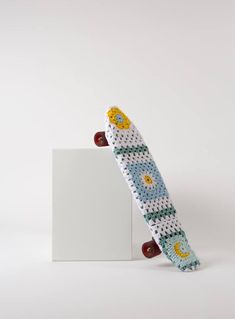 a knitted skateboard sitting on top of a white board holder next to a wall