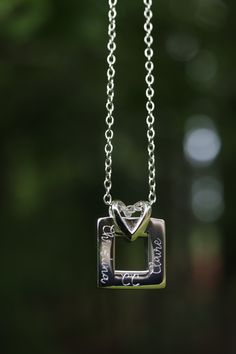 a silver necklace with a square shaped object hanging from it's side