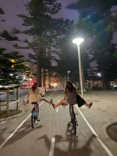 two girls riding bikes in the street at night