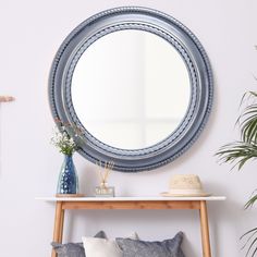 a blue round mirror sitting on top of a wall next to a wooden table with pillows