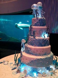 a three tiered cake with sea animals on it in front of a fish tank