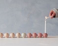 a person lighting a candle in the middle of a row of small balls with candles