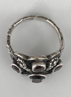 This ring is made up of four red garnet stones, the center one is red, the four on its either side are oval. They are all bezel set. Tiny silver flowers jut out of the center stone and separate the four oval stones. The band is ornately etched and it continues all around the ring. It is smooth and comfortable to wear. the underside of the ring is also quite pretty. The It is a size 5 and is in wonderful antique condition. Please see all photos for details, as well as condition. Thank you for loo Silver Ruby Ring With Three Stones In Oval Shape, Silver Three-stone Ruby Ring, Formal Silver Ruby Ring With Three Stones, Silver Ruby Ring With Three Stones, Formal Silver Ruby Three Stone Ring, Victorian Silver Ring With Garnet, Victorian Style Garnet Silver Ring, Victorian Garnet Silver Ring, Silver Ruby Ring With Rose Cut Diamonds