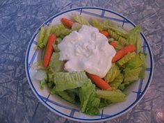 a bowl filled with lettuce and carrots covered in ranch dressing on top of a table