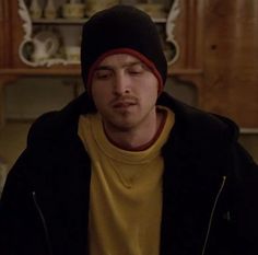 a young man wearing a beanie and looking at his cell phone in the kitchen